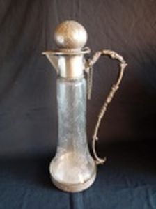 Claret jug em vidro lapidado com folhagens, guarnições em metal prateado cinzelado. Necessita pequena solda da alça na base. Alt. 38cm.