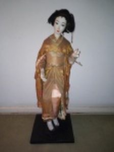 "Maiko-San" Artesanato de boneca com corpo em tecido, rosto, mãos e pés em gesso. kimono em tecido de seda, representação de nativa da Terra do Sol Nascente. Base de madeira. No estado com quebrados. Alt total 95cm.
