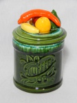 Pote em cerâmica verde vitrificada, tampa com frutas e verduras moldadas na pasta. Dois leves bicados na tampa. Alt. 21cm.