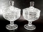 Par de porta confeitos de pé alto em demi cristal ricamente decorados por elementos geométricos e flores em relevo além de fuste sextavado. Medem 14,5 cm de altura por 9 cm de diâmetro cada.
