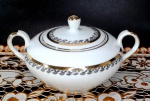 PORCELANA STEATITA - Açucareiro em porcelana branca com pintura em ouro nas alças e na pega da tampa além de arabescos em tom prata. Mede 8,5 cm de altura por 15 cm de uma alça a outra.