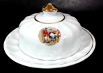 PORCELANA RAMI - Manteigueira em porcelana branca canelada decorada por cena galante em policromia e filetação dourada (com desgastes). Mede 7,5 cm de altura por 13,5 cm de diâmetro.