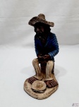 Escultura de preto velho sentado em barro com policromia, assinado Natalício Leal - Caruaru. Medindo 23,5cm de altura.