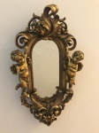 Espelho oval decorado com dois anjos em moldura no tom dourado em resina. Med. 42x25 cm.