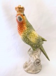 Estatueta de pássaro com coroa, repousando sobre tronco, confeccionado em porcelana. Med. 21 cm. 