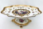 Belíssima Fruteira de pé alto, em porcelana bege, decorado com cena romântica e rosas. Flores em relevo e dourações. Med. 32x21 cm. Alt. 13 cm.