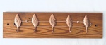 Cabideiro em Pinho de Riga com cinco ganchos representando folhas em metal no tom cobre. Med. 51x13 cm.