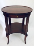 Mesa de canto oval executada em madeira nobre, contendo uma gaveta com puxador em bronze e um estágio. Quatro pés com trabalho canelado. Med. 74x54x43 cm.