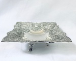 Lindo centro de mesa em metal decorado com arabescos em relevo e apoiado sobre três pés. Med. 30x22 cm.