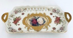 Delicado Centro de mesa em porcelana bege decorado com rosas e detalhes em ouro, flores em relevo, borda com vazados e duas pegas laterais. Med. 30x14 cm. Alt. 4 cm.