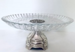 Belíssima Fruteira em vidro, borda com recortes ondulados, base e parte central em metal decorado com relevos, apresenta imperceptível bicado em uma das pontas da borda. Med. Diâm. 37 cm. Alt. 16 cm.