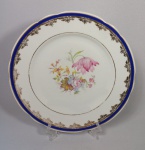 Belíssimo prato decorativo em porcelana Real com decoração floral, borda com detalhes em azul e ouro. Med. Diâm. 23 cm.