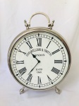 Relógio de mesa cromado com mostrador em algarismos romanos, `Sir William & Smith, London`, funcionamento à pilha. Funcionando. Med. 50x40 cm. 