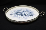FAIANÇA EUROPÉIA - Bela bandeja em faiança com rica decoração floral policromada, elegante galeria vazada em metal espessurado a prata com alças laterais, elevada por 4 pés vazados. Med. 7x43x35 cm.