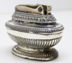 COLECIONISMO - Isqueiro de mesa com capa em metal espessurado a prata, decorada com godrões, da marca ROBSON do modelo QUENN ANNE. Med. 7x5x5 cm. Possui amassados.