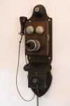 Antigo telefone americano de parede. Caixa em madeira com guarnições em metal e baquelite. Alt. 75cm. não testado.