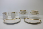 PORCELANA  - Lote de par de xícaras, 2 pratos para biscoitos curvos, 2 leilteiras em tom bege com borda dourada e coroa. Maior 24x13 cm e menor 6x9 cm.