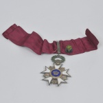 BÉLGICA. Order of the Crown; Oficial. 42,4x60,5mm. Instituída em 1897, a medalha da Ordem é uma cruz maltesa branca esmaltada com raios retos, em ouro. O disco central no anverso apresenta a coroa de ouro sobre fundo azul esmaltado; o disco central reverso tem o monograma face-a-face L (para o rei Leopoldo II) em fundo azul esmaltado. A medalha é suspensa a partir de uma grinalda de louro e folhas de carvalho esmaltadas em verde.