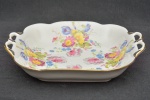 Petisqueira em porcelana esmaltada branca com decoração floral policromada e realces dourados. Marca de sua manufatura em sua base. Possui duas alças laterais. Em perfeito estado. Medida: 21 cm x 19 cm