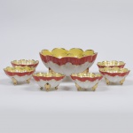 Cerâmica Santana, Pedreira - SP. Belíssimo conjunto para sobremesa em porcelana nacional, modelada em forma de concha, farta decoração de motivo vegetalista em pintura a ouro, flores em policromia, e faixas nas tonalidades vermelha e amarela, assente sobre três pés curvos terminados em voluta dourados. Composto de um(01) bowl e cinco(06) tigelas. Apresentam marca de manufatura no verso. Meds.: 10 x 21 cm; 5 x 11 cm. Bowl: (diâmetro maior da borda: 20,5 cm e altura 11,5 cm) 