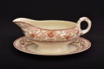 Molheira com presentoir  em seu padrão chamado DORSET feita em Stoke, Staffordshire, Inglaterra, na década de 1930. Este padrão em tom marrom e cor de marfim em porcelana tem rosas rubi e guirlandas  policromadas, grinaldas com folhas e volutas marrons e flores verde-limão conectam o padrão. Uma pequena faixa marrom floral e quadrada na borda e outra faixa interna de figuras geométricas perto da borda. Esta é em porcelana e é um item muito substancial, bem feito. Está em muito bom estado. Marca de sua manufatura em sua base. Medida: Molheira 9 cm altura x 9 cm largura x 19,5 cm comprimento; Presentoir: 20,5 cm comprimento x 14 cm largura.