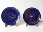 Lote de dois pequenos pratos decorativos azul cobalto com frisos dourados, acompanha suporte. MED: 12cm diâmetro.