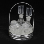 Galheteiro com base de metal e cinco frascos de vidro moldado.