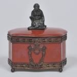 Antiga caixa de fina porcelana, na cor terracota, adornada por metais, encimada por figura oriental, med. 11 x 13cm.