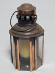 Antiga pequena lanterna na forma de lamparina, estrutura em metal cobreado, formato sextavado com placas de vidro, interior para 1 vela, parte superior com sulcos para fumaça. Desgastes do tempo. Alt. com alça 23cm.