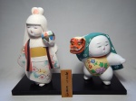 Duas estatuetas japonesas em cerâmica policromadas representando menina com bola e menina com máscara de dragão. Selo de origem no fundo, bases de madeira. Alts. 33 e 23cm.