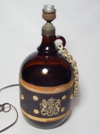 Abajur confeccionado na forma de garrafão de vinho em vidro âmbar, aplicado com brasão do Reino Unido em plástico ao centro, ornamentado com corrente na alça. Não acompanha cúpula. Alt. 37cm.