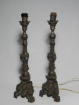 Par de tocheiros em metal amarelo, estilo Dom João V, base em 3 pés com saia ornamentada por folhagens e medalha, haste no estilo torneado e em volutas, parte superior finalizada por coroa. Não acompanha cúpulas. Alt. 57cm.