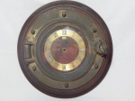 Relógio de parede adaptado em escotilha em metal amarelo, emoldurado por placa em madeira, numerais romanos sobre cinturão metálico, inscrições "Anju". Falta todo o maquinário de funcionamento. Diâm. 30cm.