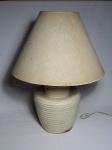 Abajour em faiança bege moldado na pasta com decoração imitando palha trançada, cúpula em acetato revestido por tecido. Apresenta craquelado na faiança, cúpula em acetato revestida em tecido. Alt. 64cm.