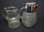 Duas refresqueiras em vidro moldado com formato rajado, borda e alça em metal prateado, uma com compartimento para gelo. Alts. 21 e 26cm.