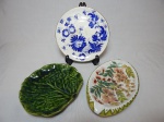 Três peças: a) ZAPPI, São Paulo - Prato decorativo em porcelana nacional, borda em douração, centro decorado com flores azuis pintadas à mão. Centro com fios de cabelo. Diâm. 19cm. b) Cinzeiro oval em porcelana branca, centro aplicado com flores e folhagens pintadas à mão. Assinada por Moema. Marcada REAL SÃO PAULO. 14 x 22cm. c) LUIZ SALVADOR - Petisqueira em cerâmica vitrificada no formato de folha de couve. Diâm. 17cm.
