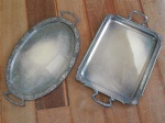 Duas bandejas com alças em metal espessurado a prata: a) Retangular, borda moldada com volutas e concheados, marcada Wolff. 54 x 32cm. b) Formato oblongo, borda moldada com volutas e acantos. 30 x 53cm.