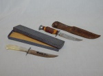 Duas facas: a) Cabo em resina imitando chifre de veado, ponteira do punho em alumínio, lâmina com serra na ponta. Manufatura Mundial, inox. bainha de couro. Comp. da faca 24cm. b) Cabo em resina imitando madrepérola, lâmina gravada "Querência dos Maragatos". Manufatura Prestil, inox. Comp. 25,5cm.