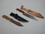 Duas facas: a) Cabo de madeira torneada, lâmina gravada Estado-Maior do Exército, Brasil. Manufatura Prestil, modelo Jaguar. Bainha de couro e metal. Comp. da faca 27cm. b) cabo de resina moldado com cena de caça e saca-rolhas. Bainha de couro e metal. Brinde de Luiz Caetano - Leiloeiro. Comp. da faca 30cm.