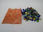 Saco com dezenas de bolas de gude em vidro, algumas multicoloridas. Tamanhos variados.