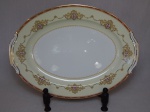 NORITAKE - Travessa oval em porcelana japonesa, borda com esmaltagem bege, medalhões de buquê de flores circundado por volutas e acantos interligados por guirlandas, friso grená. Marcado no fundo. 41,5 x 31cm.