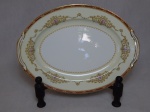 NORITAKE - Travessa oval em porcelana japonesa, borda com esmaltagem bege, medalhões de buquê de flores circundado por volutas e acantos interligados por guirlandas, friso grená. Marcado no fundo. 30 x 22cm.