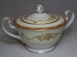 NORITAKE - Açucareiro em porcelana japonesa, borda com esmaltagem bege, medalhões de buquê de flores circundado por volutas e acantos interligados por guirlandas, friso grená. Marcado no fundo. Pega em pinha. Alt. 11cm.