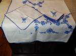 Toalha e 6 guardanapos em linho branco bordado com guirlandas de flores em azul. Manchas de guardado. 135 x 145cm e 28 x 28cm.