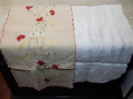 Dois caminhos de mesa: a) Cambraia de linho com vazados. Com manchas. 200 x 45cm. b) Linho bege bordado com flores coloridas. 210 x 42cm.
