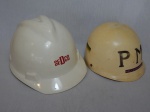 Dois capacetes, sendo um EPI da Sedco e uma réplica de brinquedo do antigo capacete da Polícia Militar. Ambos em plástico. Alts. 17 e 13cm.