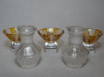 Cinco peças de cristal: a) Par de galhetas, meio bojo lapidação ponta de diamante. Alt. 9cm. b) Três cálices poloneses lapidados com facetas na tonalidade âmbar e translúcida. Selo de procedência. Alt. 6cm.