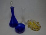 Três peças em vidro: a) Licoreira com base em vidro azul escuro, alt. total 32cm. b) Petisqueira em vidro moldado com caneluras amarelo e translúcido, 17 x 15cm; c) Porta-velas translúcido, alt. 20cm.