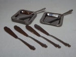Seis espátulas e 6 manteigueiras em inox, borda decorada com acantos e volutas. 8 x 8cm.