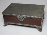 Porta jóias em madeira e metal prateado, pés e fecho vazados com volutas, tampa em metal cinzelado com paisagem. Desgastes no metal. 8 x 20,5 x 13cm.